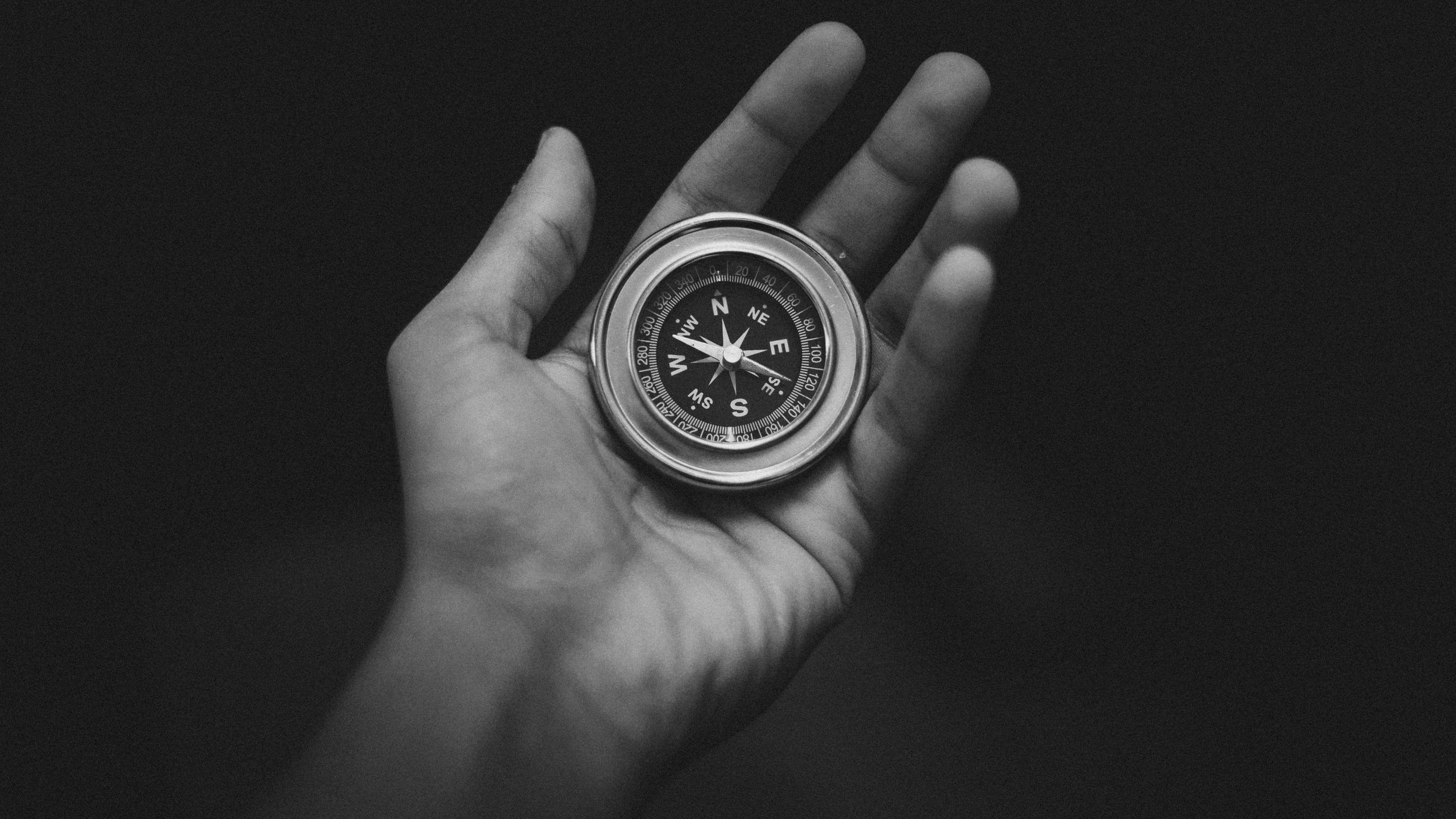 Fotografía que muestra una mano sosteniendo una brújula en blanco y negro