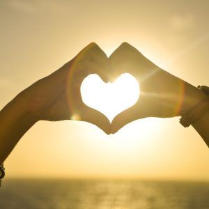Dos manos juntas haciendo la forma de un corazón por donde se refleja el sol